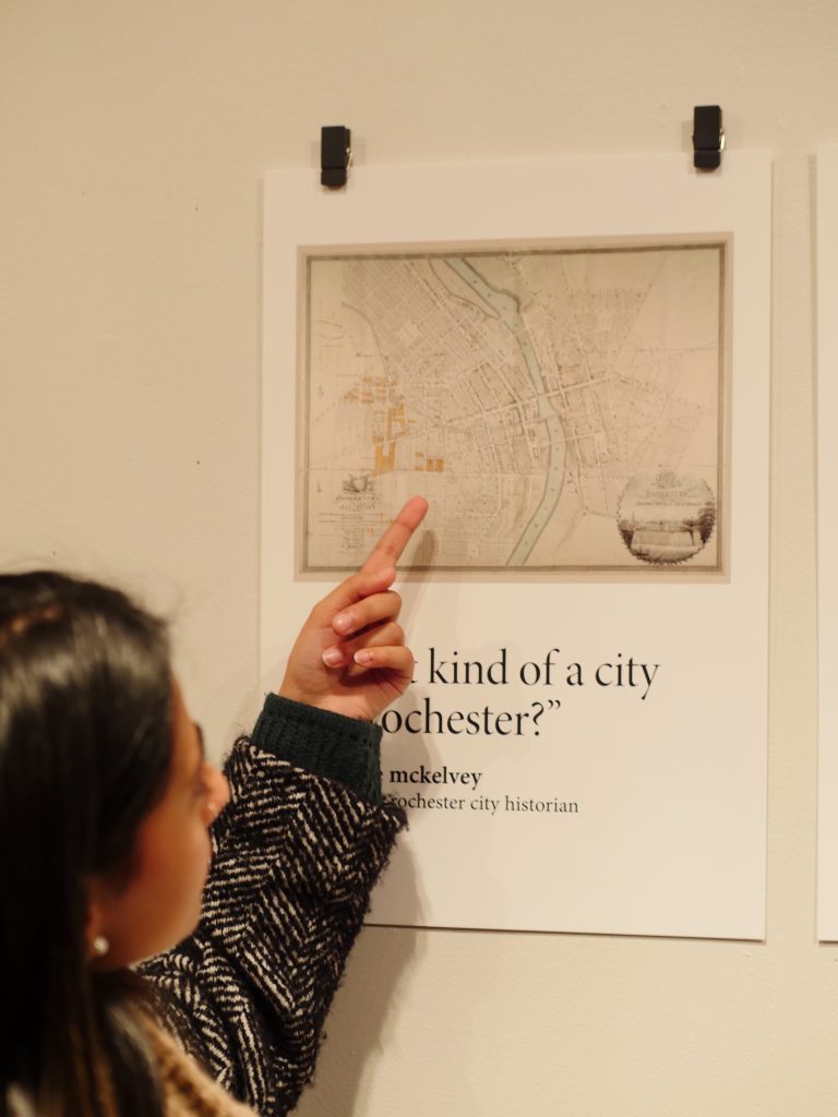 a gallery visitor points to a print featuring an old map of rochester